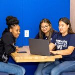 Three students in the student center looking at a laptop.